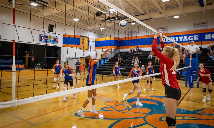Volleyball players jump toward the net to play the ball